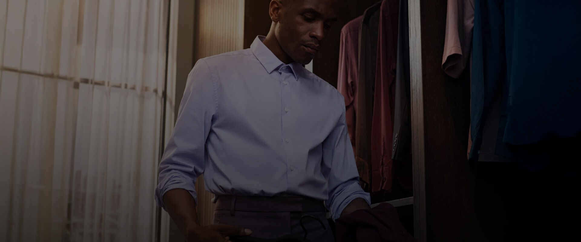 En mand i en blå skjorte står ved et klædeskab og vælger tøj.